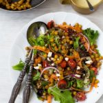 Quinoa salad with crispy chickpeas with salad servers from above on a white background.