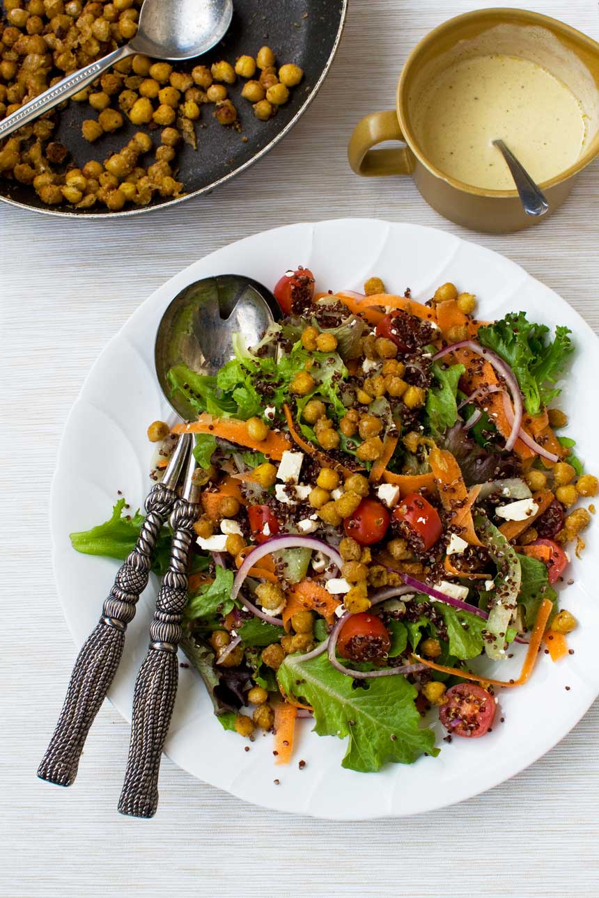 Quinoa salad with crispy chickpeas with salad servers from above on a white background.