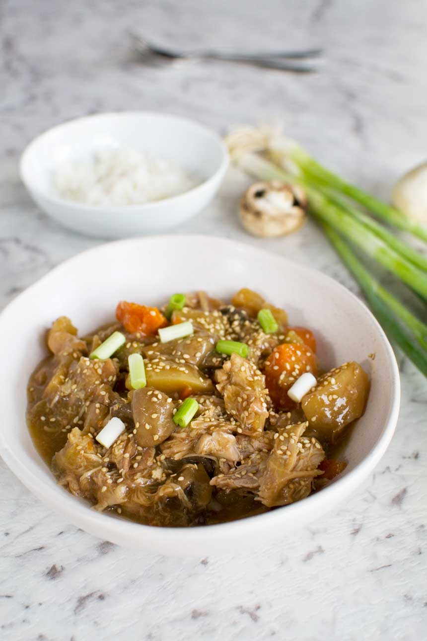 A white bowl of Slow cooker Korean chicken on a marble background with ingredients behind.