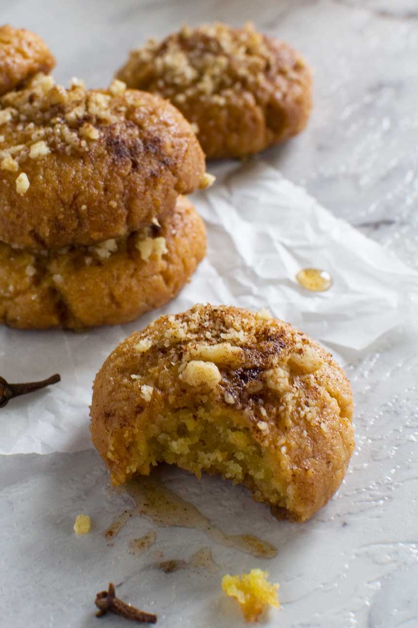 A closeup of a Greek Christmas honey cookie or melomakarona with a bite out of it and with more cookies in the background