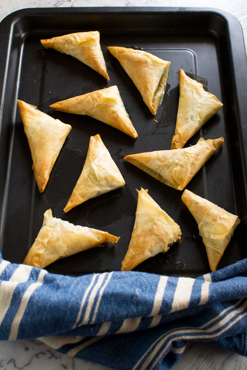 Crispy mushroom filo triangles on a baking tray from above and with a blue striped tea towel.