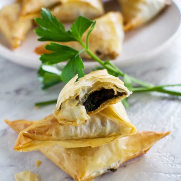 A small stack of crispy mushroom filo triangles on a marble background with more on a plate in the background.