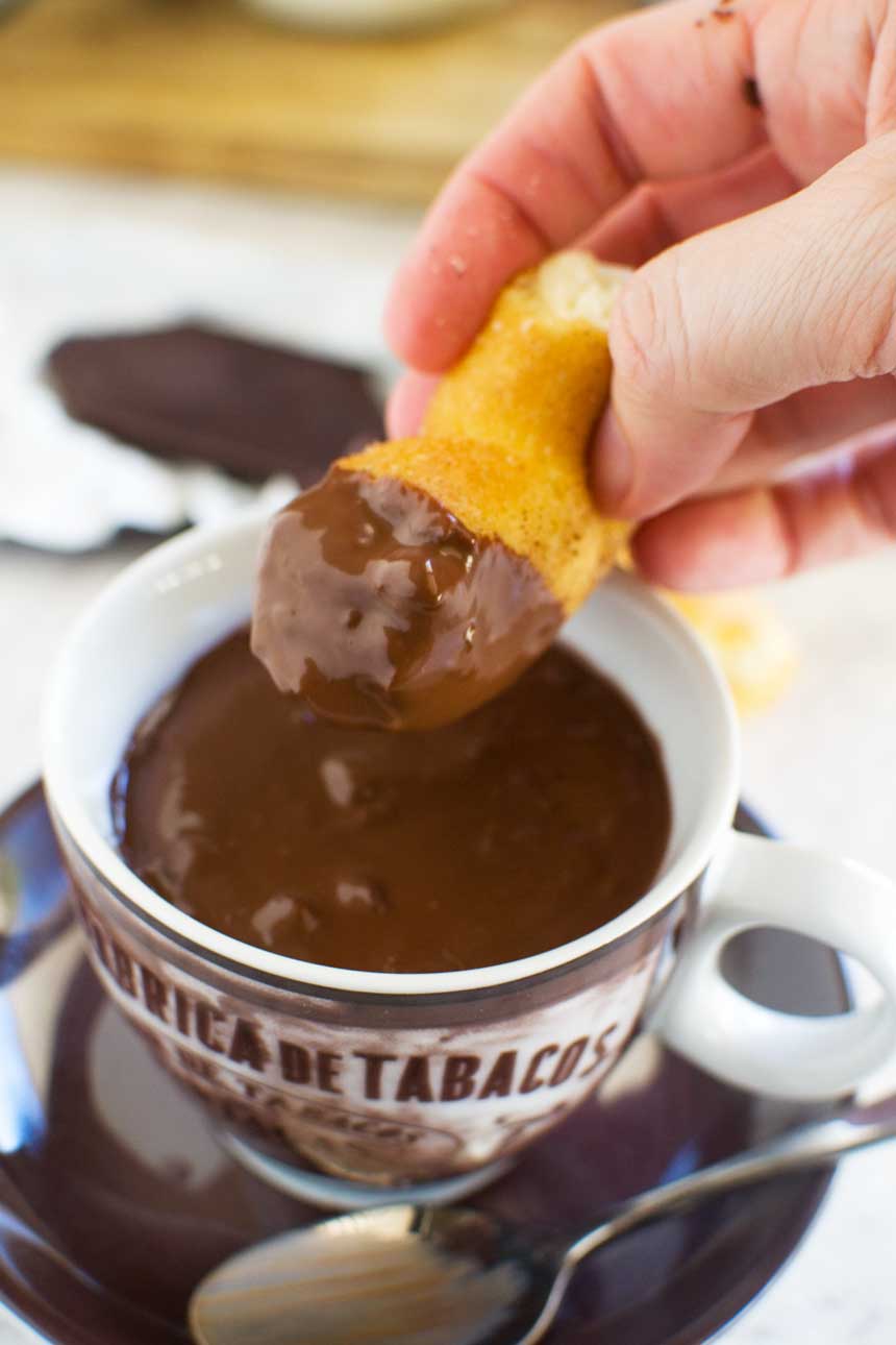 Someone dipping a churro in a brown cup of thick hot chocolate.