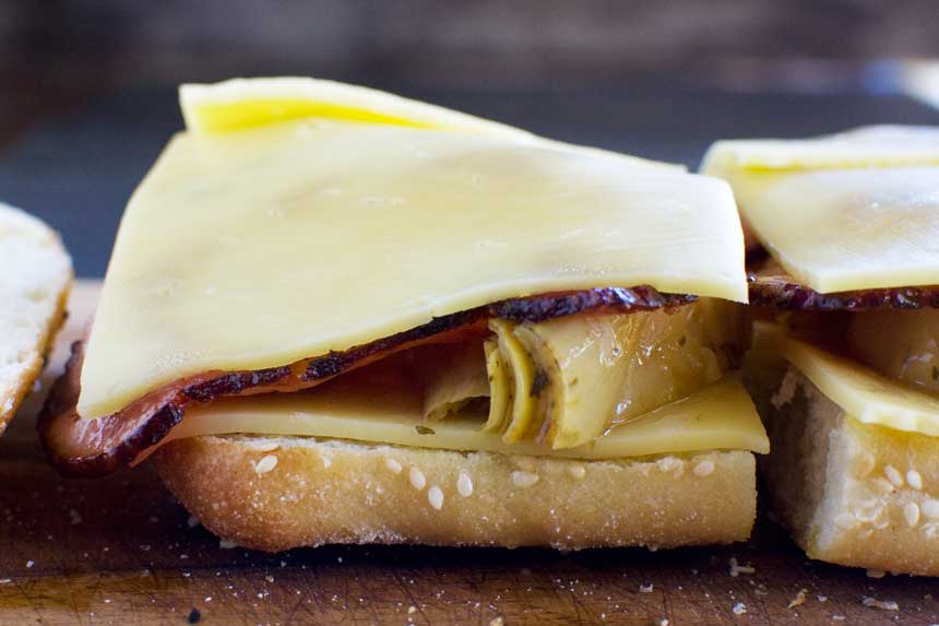 A close up of the bottom half of an artichoke grilled cheese sandwich on a wooden board.