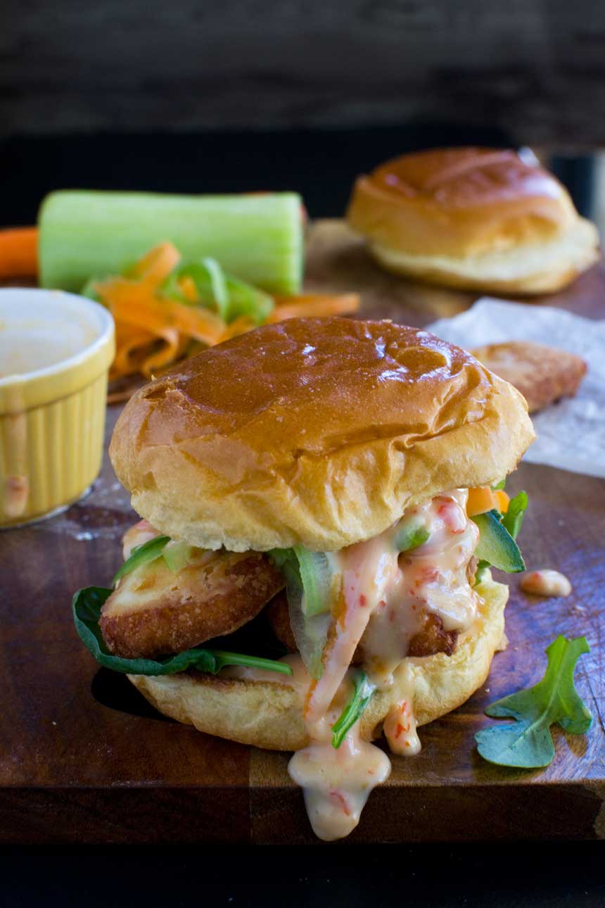 A crispy halloumi burger with sweet chilli mayonnaise on a wooden background with ingredients in the background.