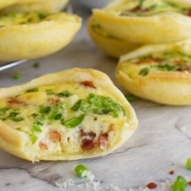 A close up of a mini quiche with a bite out of it on a marble background with other mini quiches in the background.