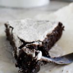 A close-up of a piece of 6-ingredient gooey Swedish chocolate cake or kladdkaka with a fork on baking paper.