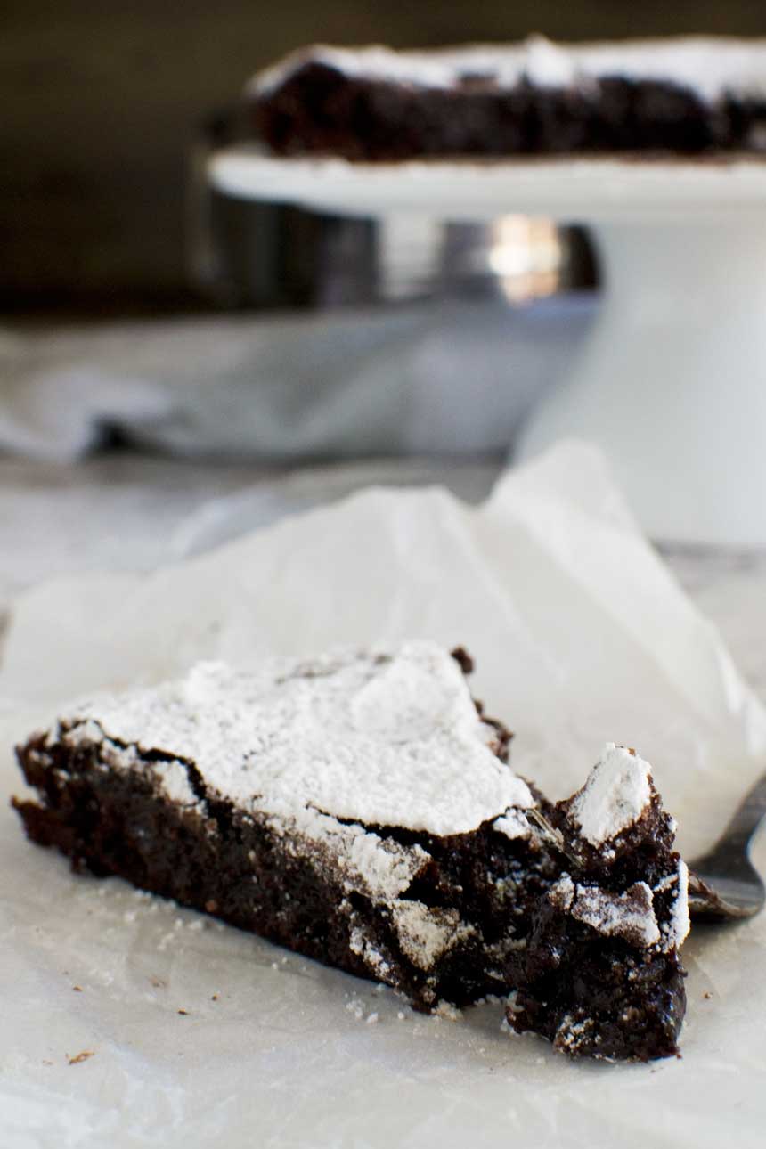 A close-up of a piece of 6-ingredient gooey Swedish chocolate cake or kladdkaka with a fork on baking paper from the side.