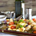 Easy baked gnocchi with sausage, peppers and tomatoes on a baking tray with ingredients in the background