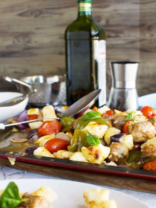 Easy baked gnocchi with sausage, peppers and tomatoes on a baking tray with ingredients in the background