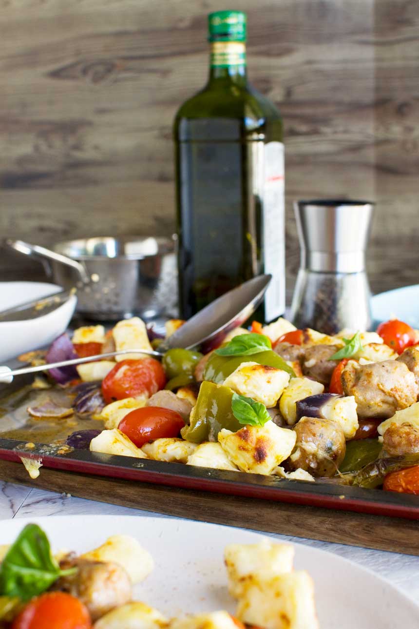 Easy baked gnocchi with sausage, peppers and tomatoes on a baking tray with ingredients in the background