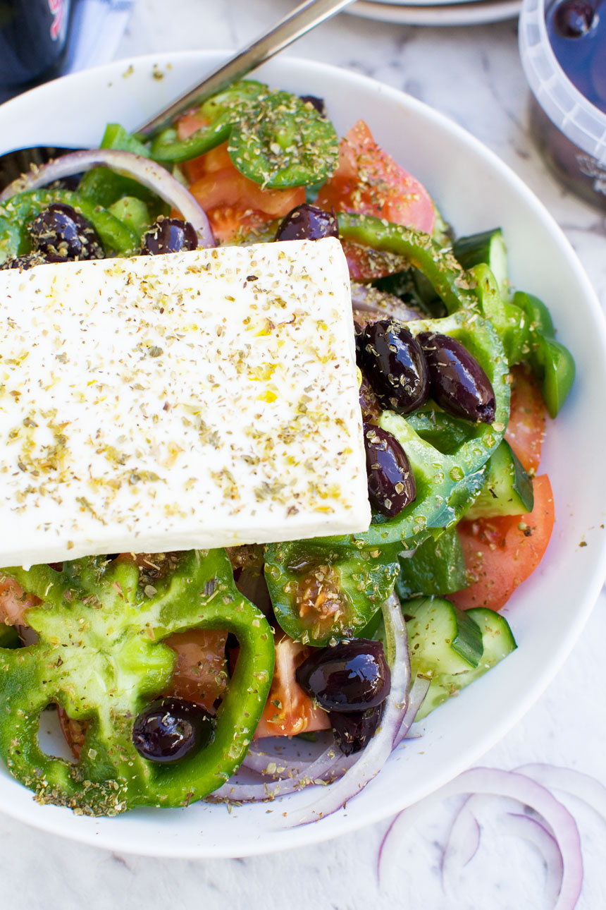 Part of A traditional Greek salad with a whole block of feta on top from above in a big white bowl.