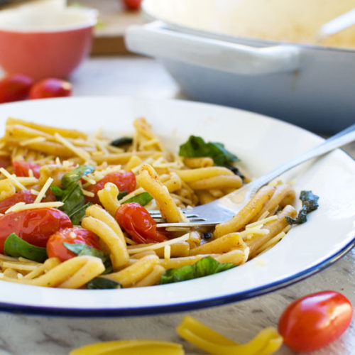 12-minute cherry tomato pasta in a white dish with a blue rim with dishes and ingredients all around and on a marble background.