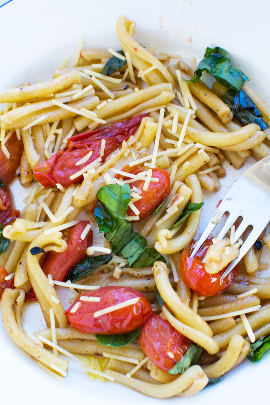 A closeup of a plate of cherry tomato pasta with a fork in it and cheese on topo.