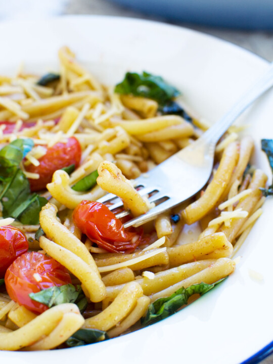 closeup of 12-minute cherry tomato pasta in a white bowl with a fork.