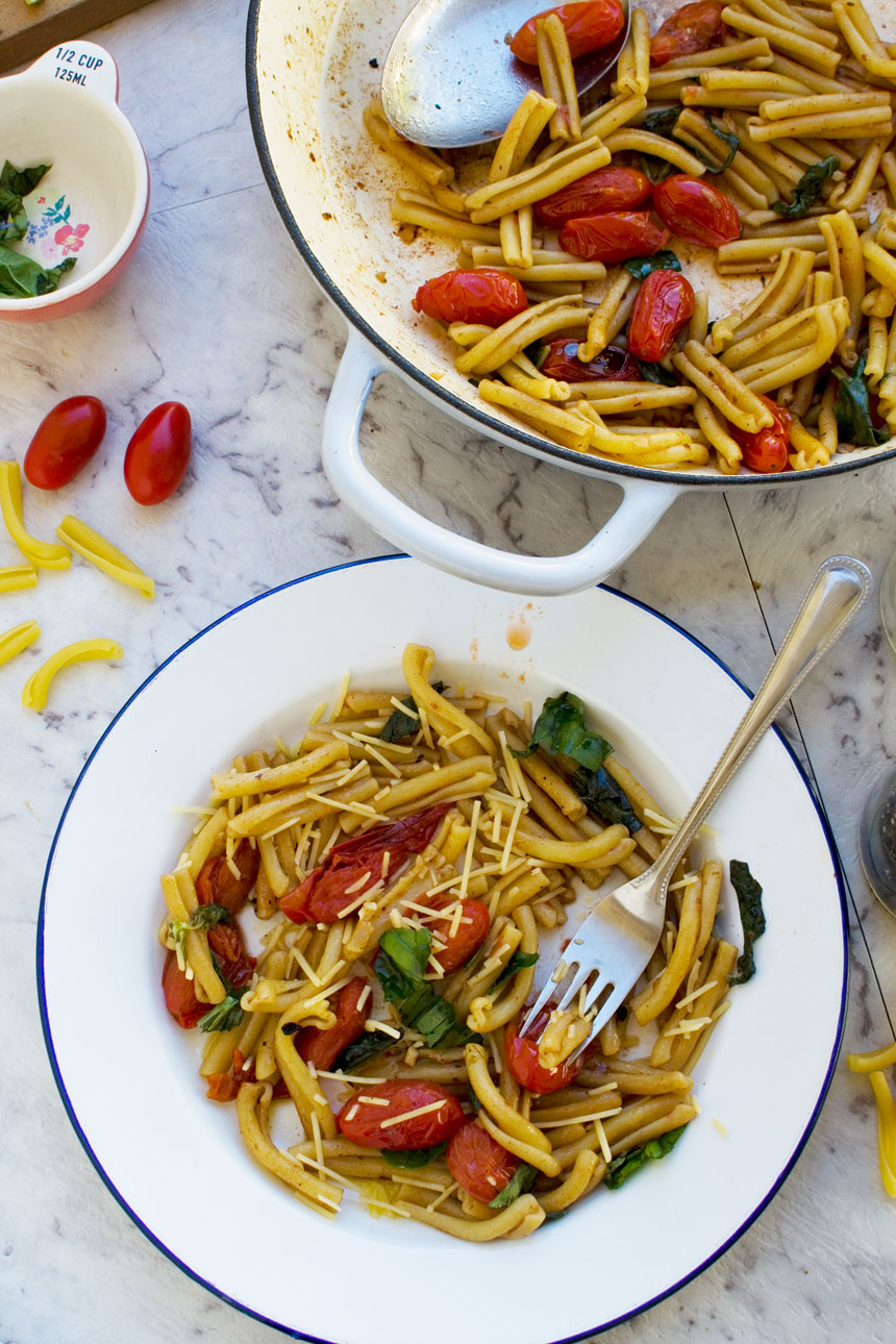 A white dish with a blue rim with 12-minute cherry tomato pasta and a fork in it and with a baking dish next to it.
