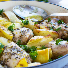 One pan Greek baked chicken and potatoes with a Greek salad in the background