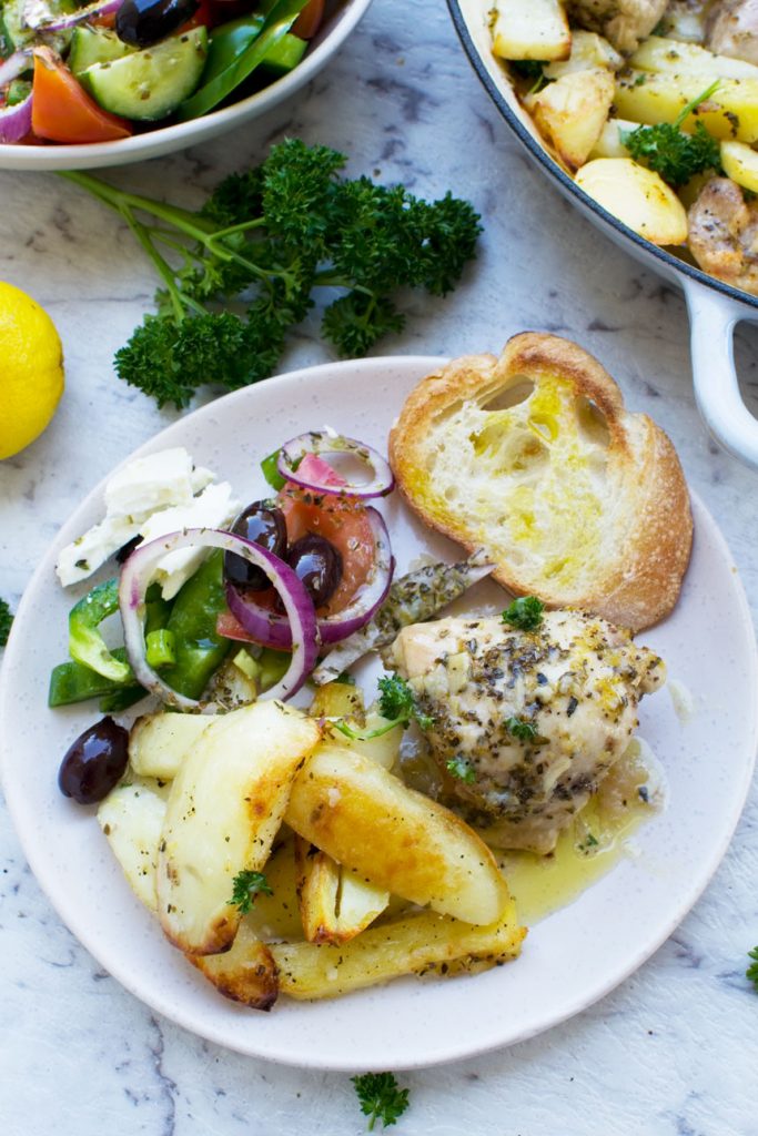 A plate of Greek baked chicken & potatoes with a Greek salad