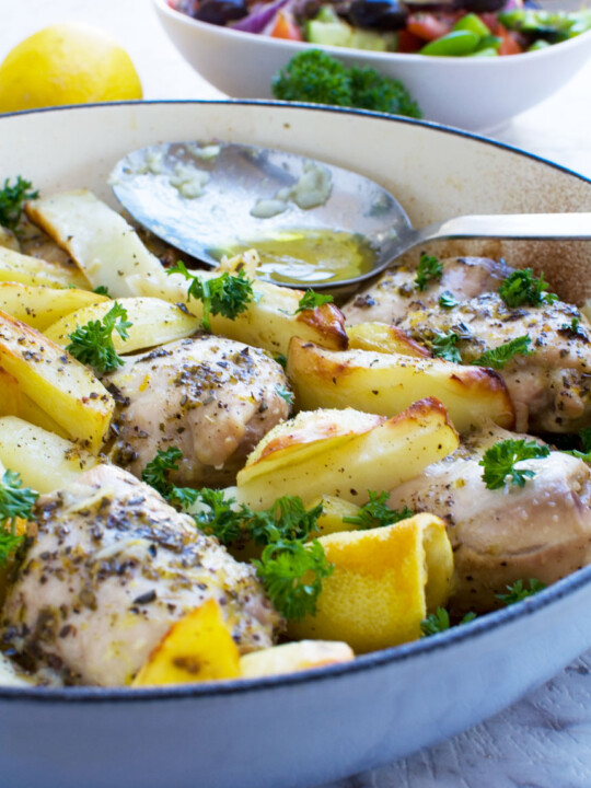 One pan Greek baked chicken and potatoes with a Greek salad in the background