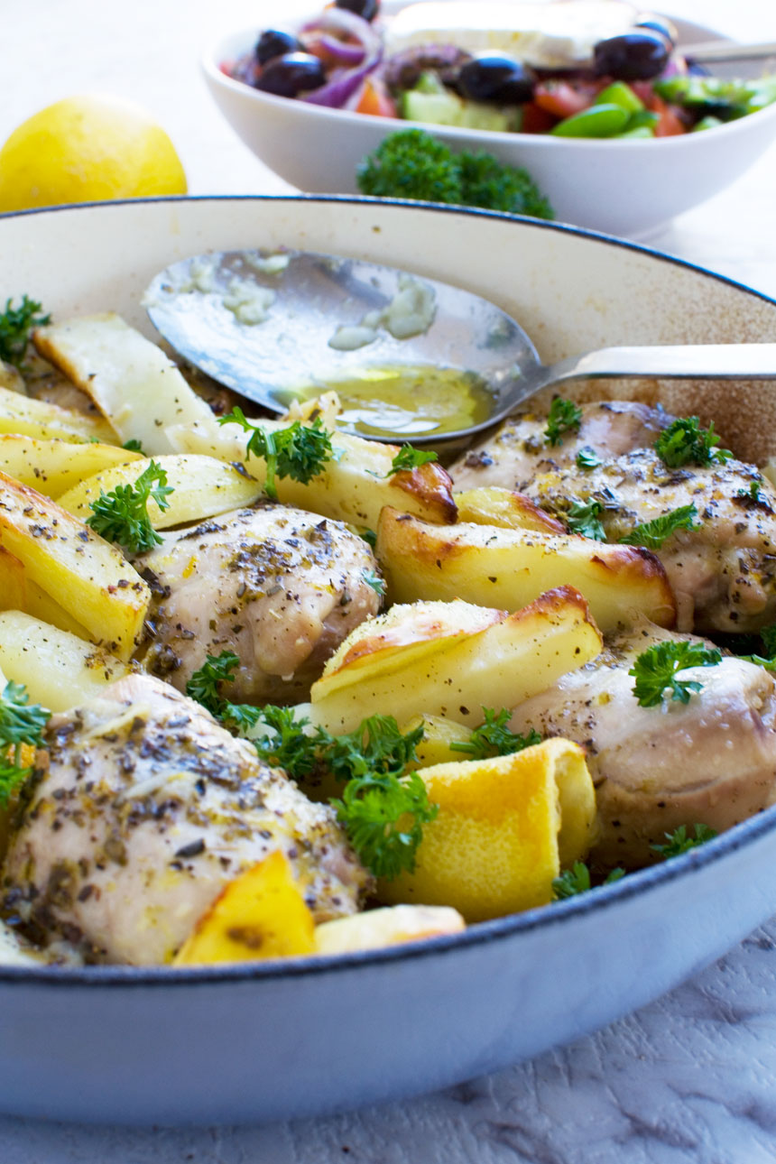 One pan roasted Greek chicken and potatoes with a Greek salad in the background