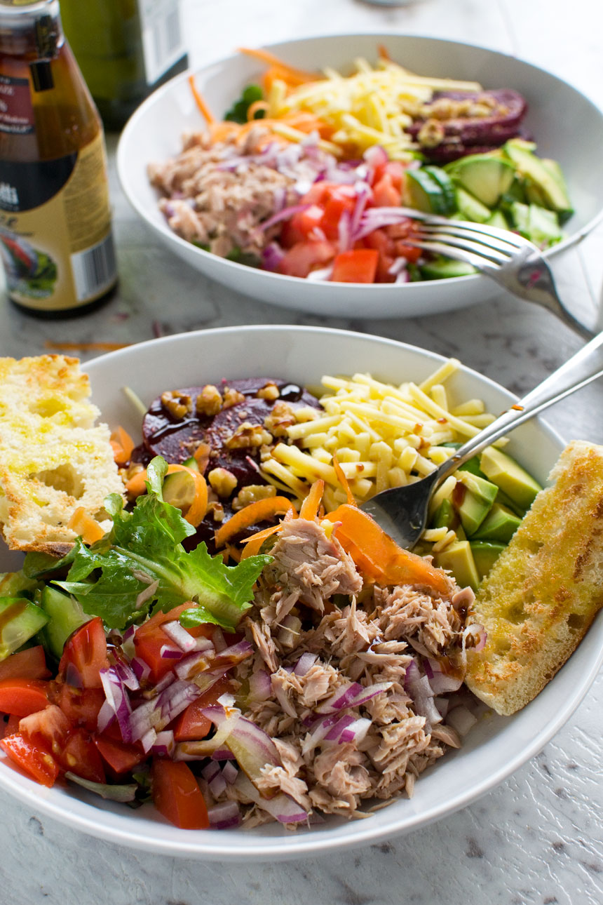 Closeup of an easy tuna salad in a white bowl with a spoon in it and with another salad and balsamic vinegar in the background.
