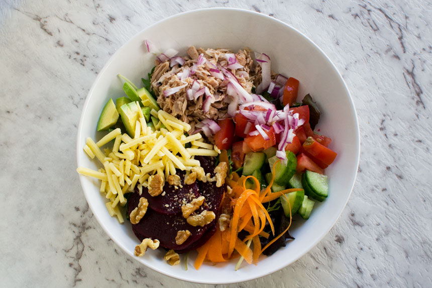 View from above of a colourful tuna salad in a white bowl on a marble background.