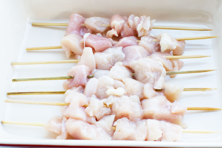 Skewers of chicken in a baking dish for making chicken satay skewers.