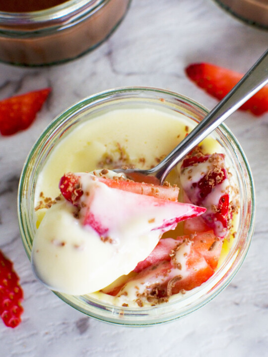 5-minute white chocolate pot de crème with strawberries in it and a spoon from above on a white marble background.