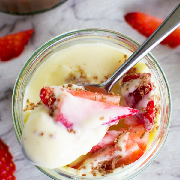 5-minute white chocolate pot de crème with strawberries in it and a spoon from above on a white marble background.