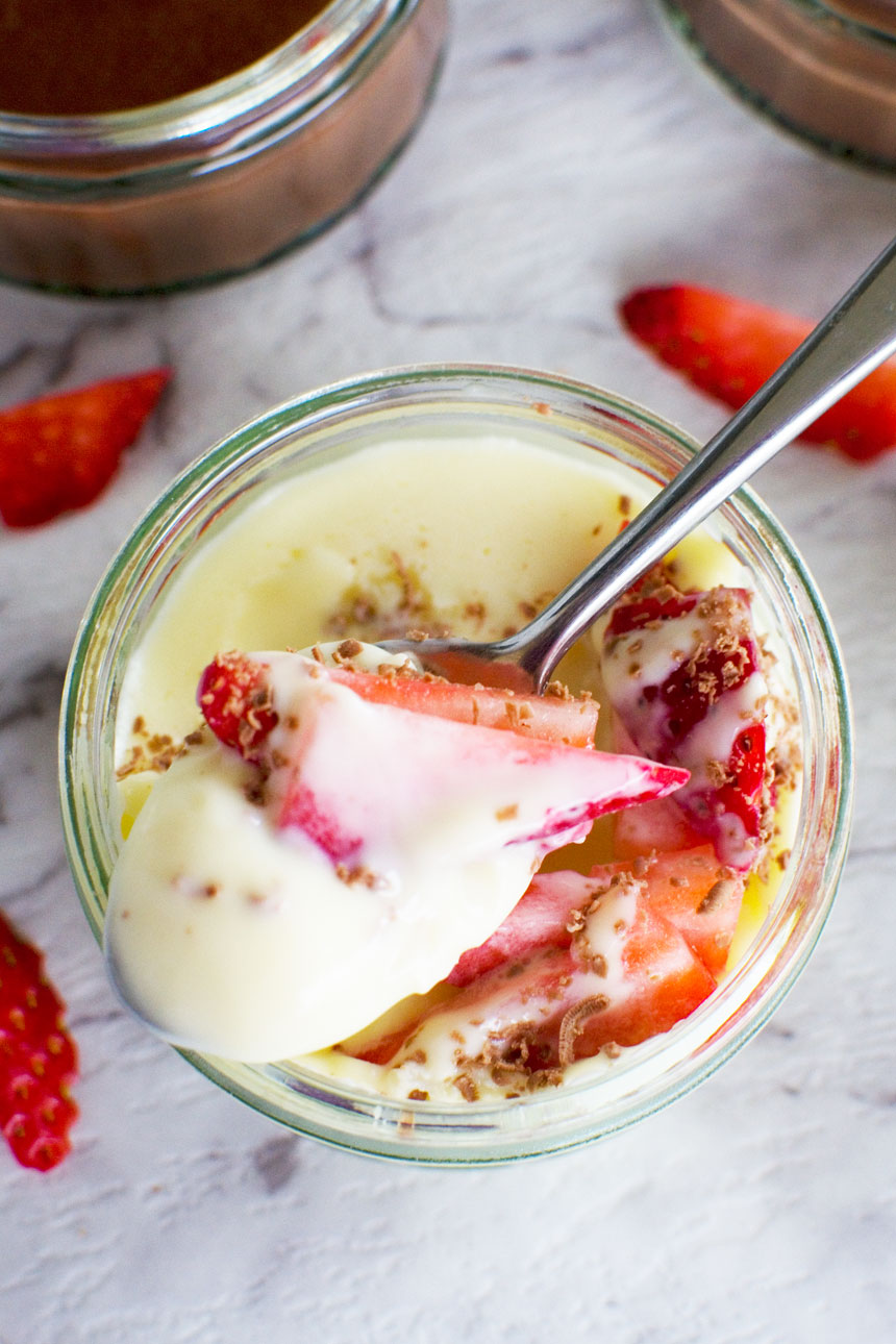 5-minute white chocolate pot de crème with strawberries in it and a spoon from above on a white marble background.