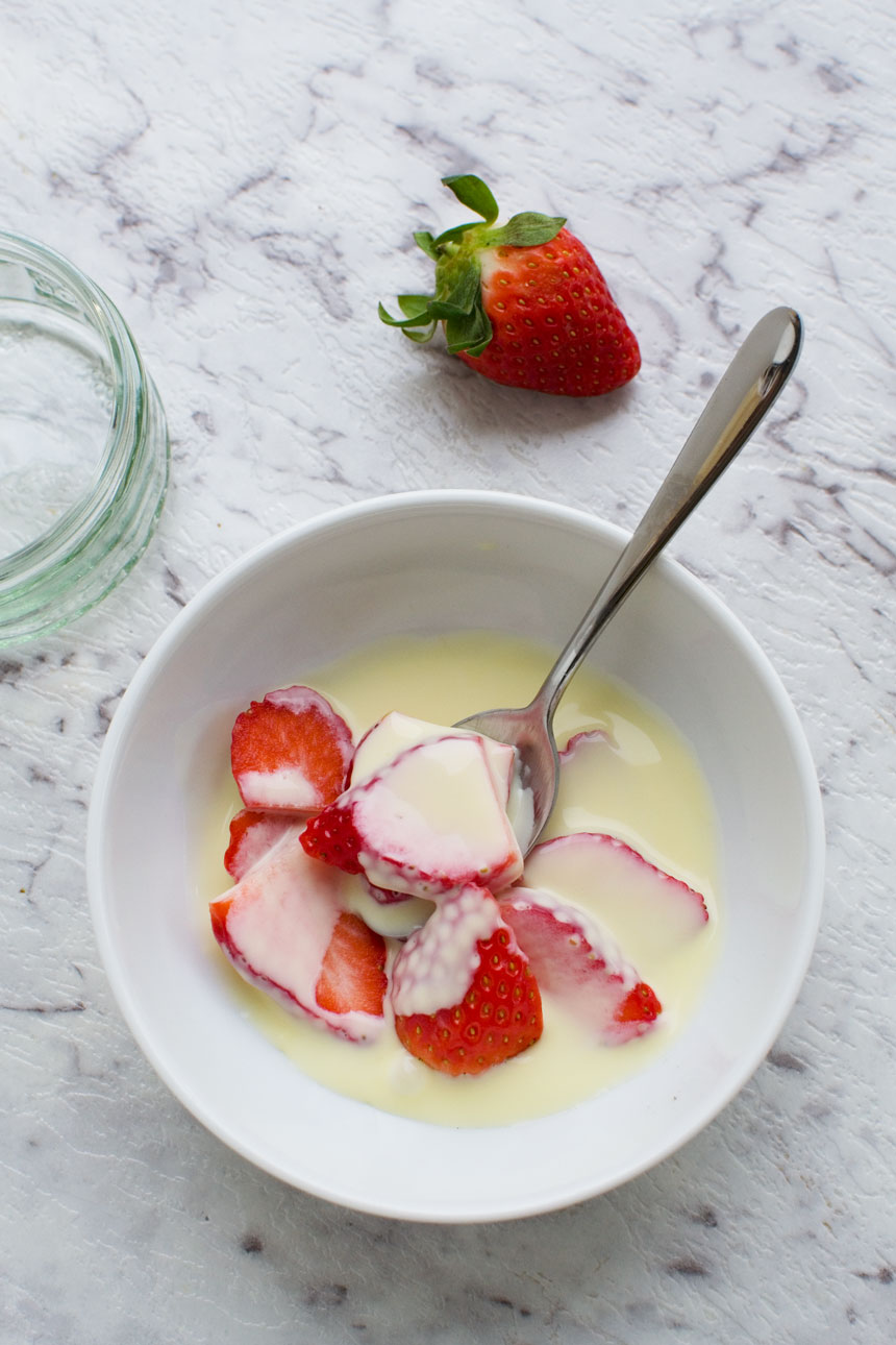 White chocolate sauce in a bowl with strawberries on a marble background.