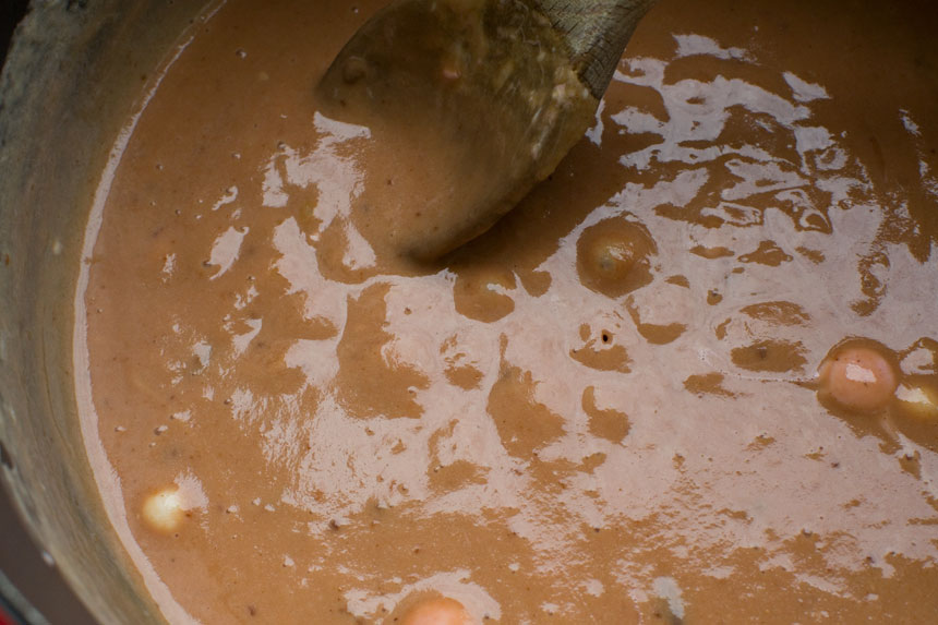 The caramel mixture for making peanut butter cheerio bars in a saucepan with a wooden spoon