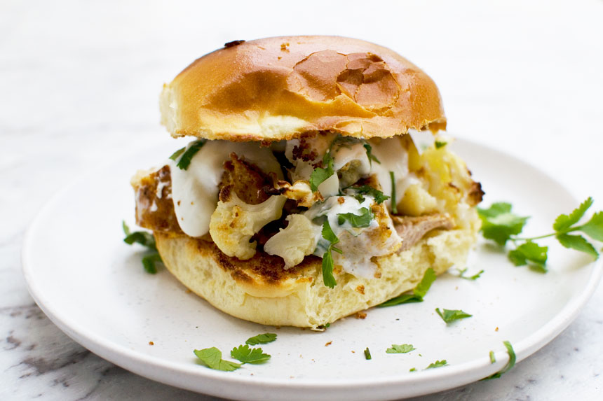 Sheet pan chicken tikka burger on a white plate with fresh herbs scattered around it.