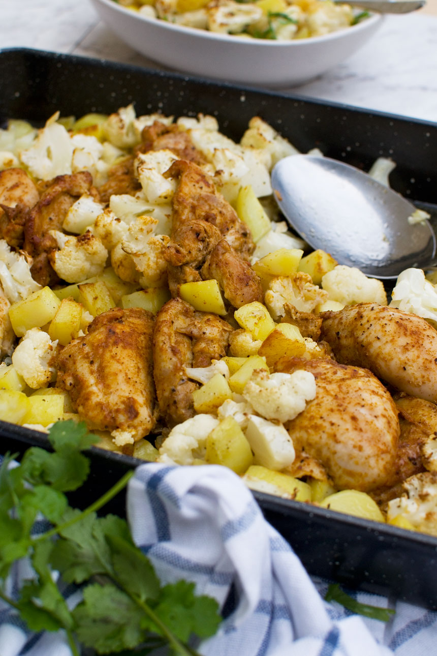 Closeup of sheet pan chicken tikka with cauliflower and potatoes from the side with a spoon in it.