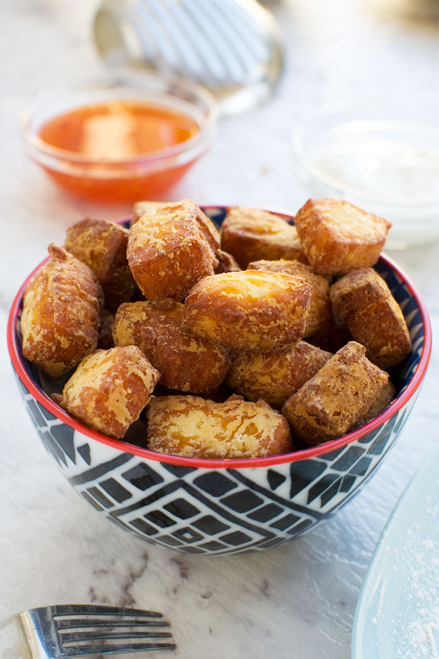 fried halloumi bites in a blue bowl up close with sweet chili sauce and greek yogurt in the background