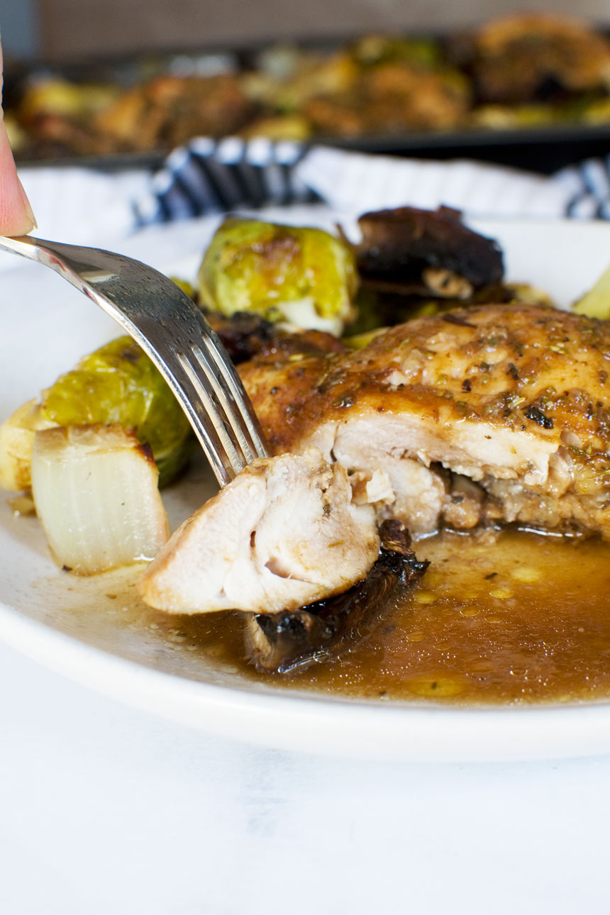 Closeup of a piece of Honey balsamic chicken on a fork with the meal in the background on a white plate