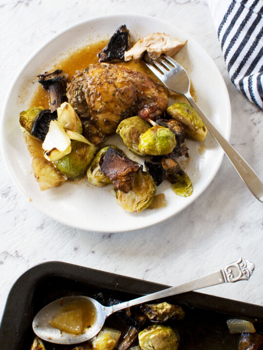 plate of Honey balsamic chicken with mushrooms and brussels sprouts from above with a striped tea towel and the baking pan at the edge of the image