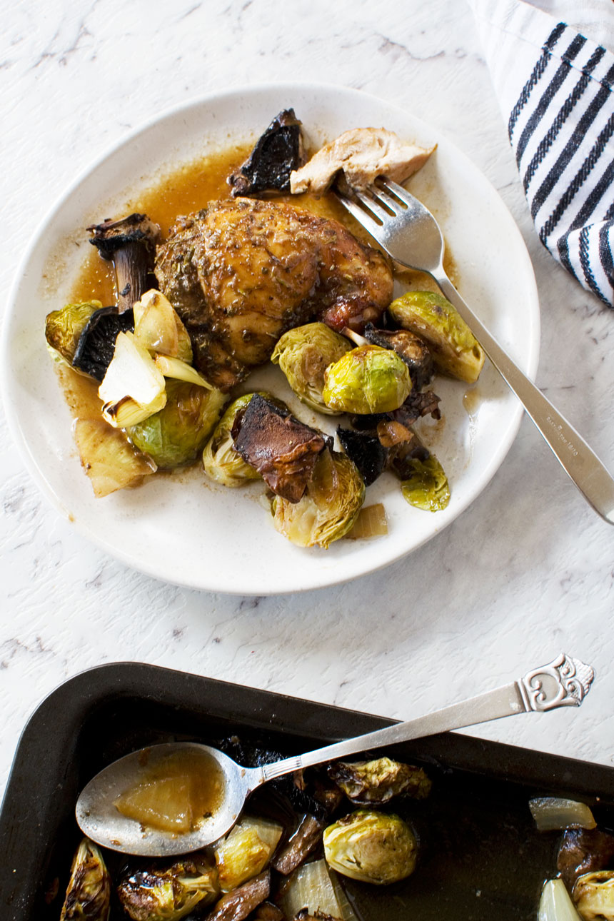 plate of Honey balsamic chicken with mushrooms and brussels sprouts from above with a striped tea towel and the baking pan at the edge of the image