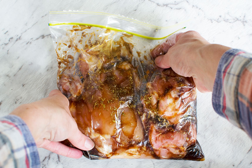 Someone\'s hands holding the Marinade for honey balsamic chicken with mushrooms and brussels sprouts in a freezer bag
