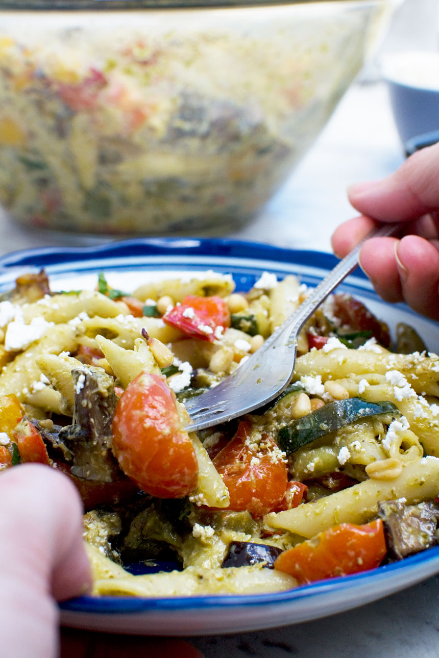 Person eating Mediterranean penne pasta salad with a fork from a blue dish