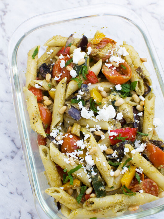 Mediterranean penne pasta salad in a clear glass container on a marble background