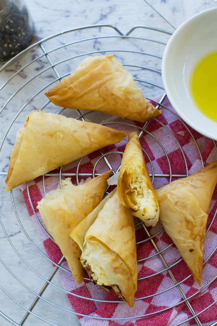 Tiropita or mini Greek cheese pies on a cooling rack and with a red tea towel underneath from above