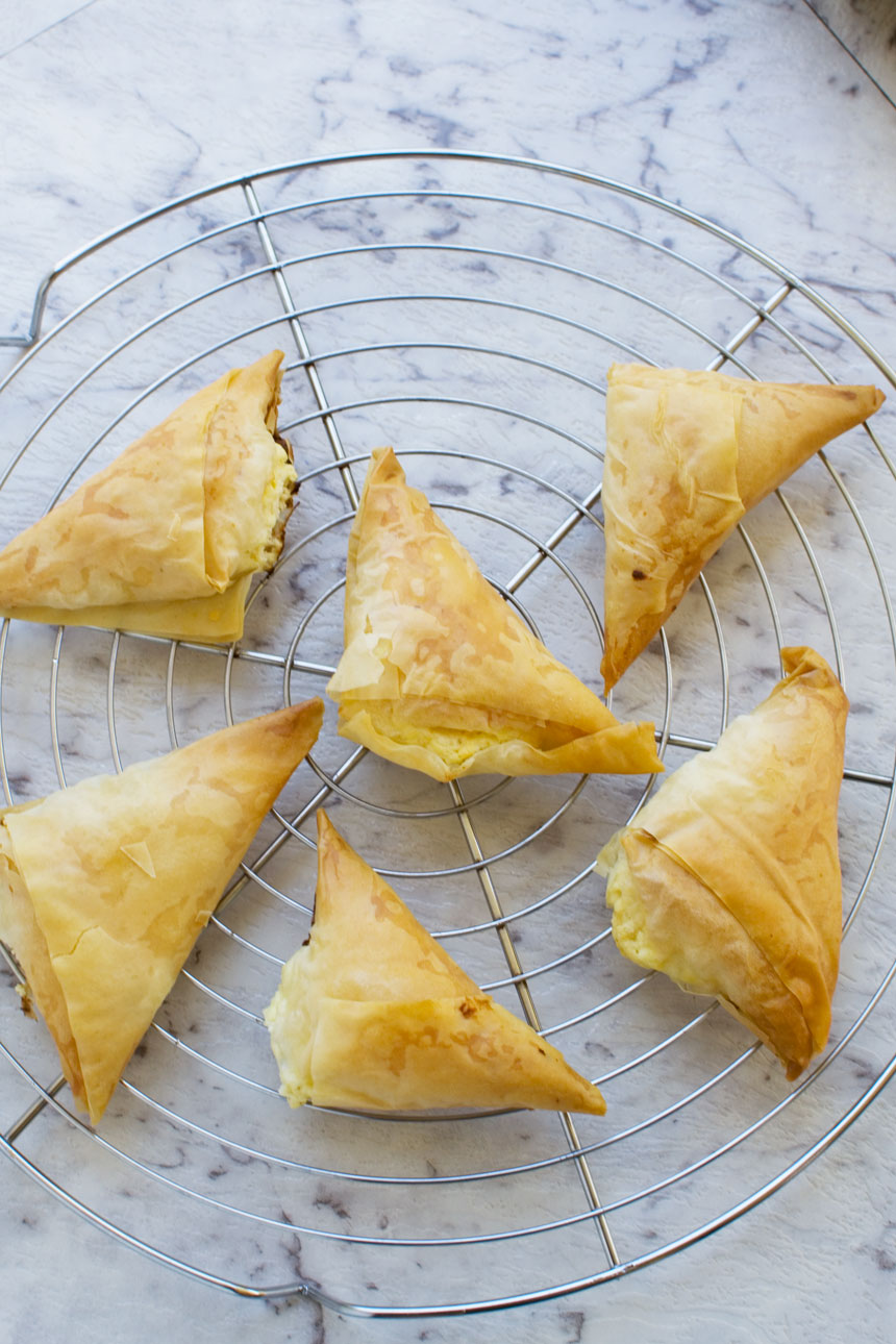 Tiropita or mini Greek cheese pies on a cooling rack and marble background from above