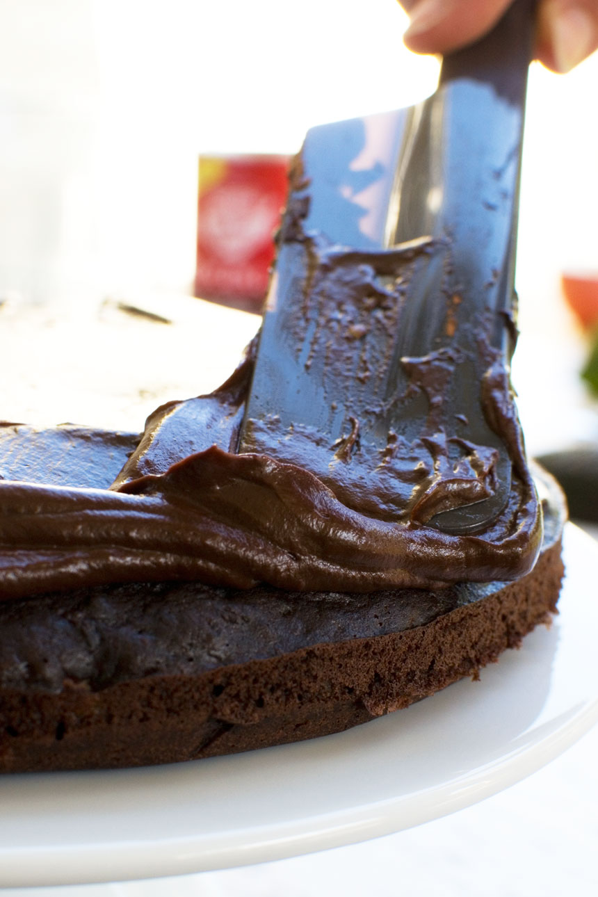 Closeup of someone spreading frosting on a 30 minute healthy chocolate cake with a spatula
