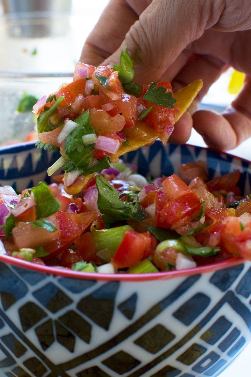 someone eating 10 minute tomato salsa with a nacho from a blue and red bowl