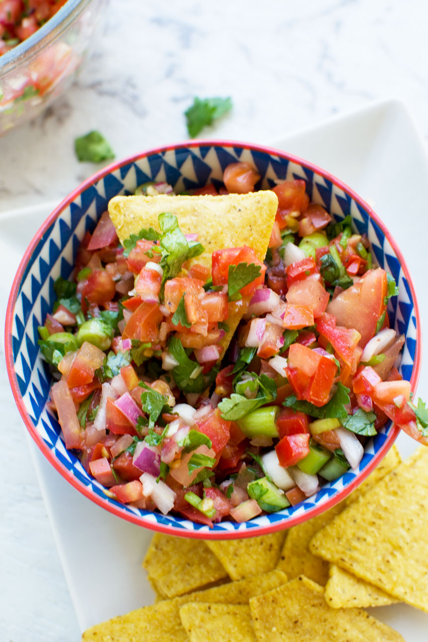 Colourful blue and red bowl of 10 minute tomato salsa with a nacho in it and more nachos around the side