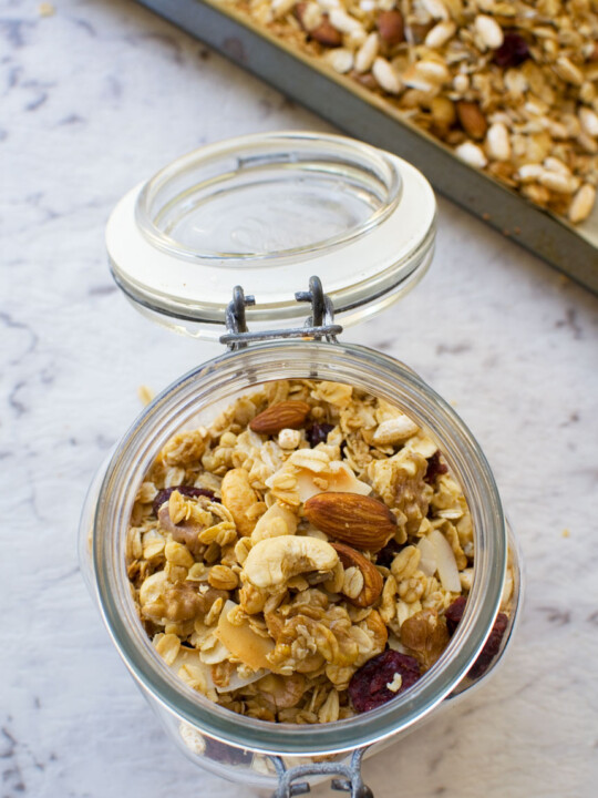 Basic homemade granola in an open glass container from above with a baking tray of granola in the background