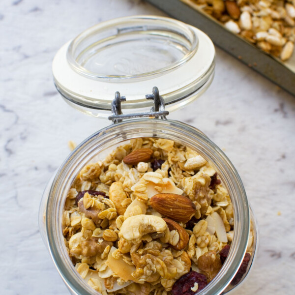 Basic homemade granola in an open glass container from above with a baking tray of granola in the background