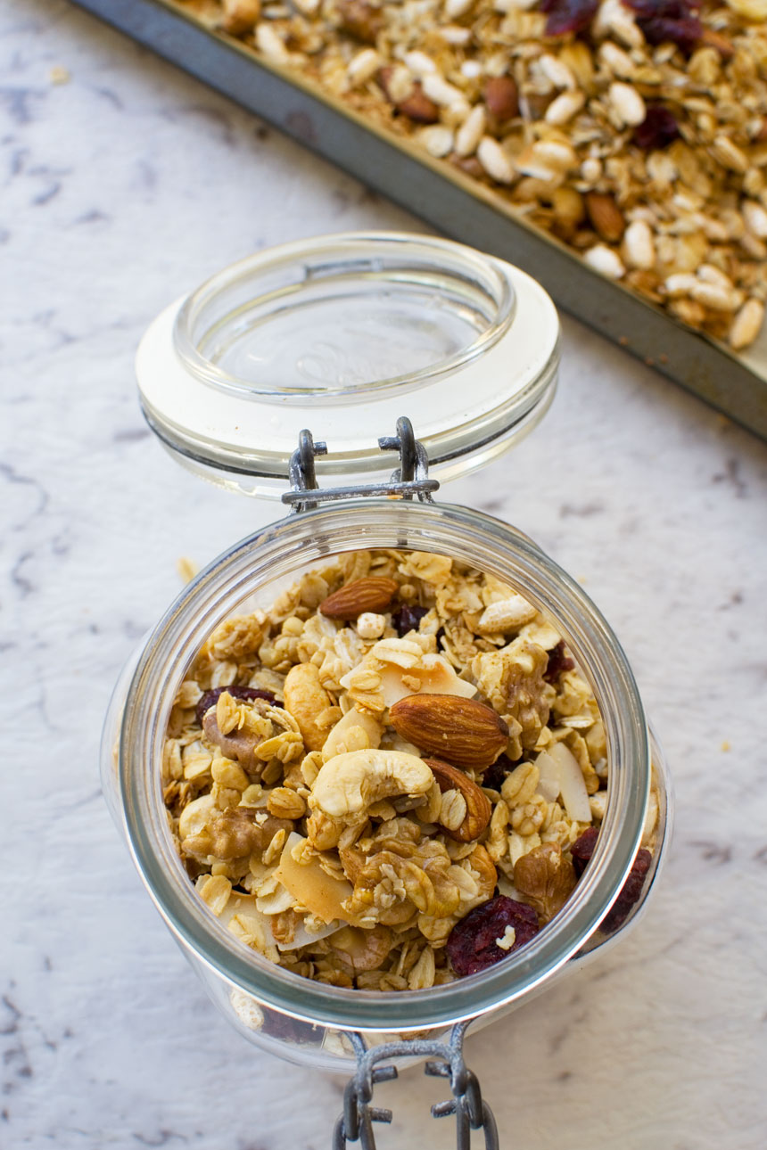 Basic homemade granola in an open glass container from above with a baking tray of granola in the background