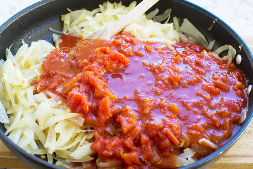 cooking onions and tomatoes in a frying pan for Greek baked fish